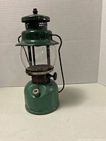 Front and side view of green metal Coleman Sportlite #242 lantern with glass globe and top vent showing wear and dents.