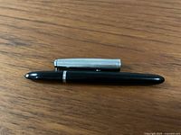 Cap removed, showing black resin barrel and brushed metal cap side by side on wooden surface