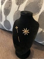 Brooch and stick pin displayed on black jewelry bust