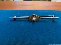 Front view of the straight bar brooch laid on blue cloth, showing entire piece.