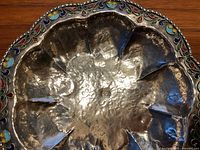 Close up of hammered silver surface and colorful enamel floral border on rim