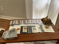 Wide view of silk cigarette silks with medal images and small country flag silks arranged on a wooden table, along with a small fabric dog figurine and two metal ashtrays.