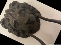 Front view of the lion head door knocker showing detailed facial features and mane with attached curved handle knocker.