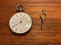 Front view showing white enamel dial, Roman numerals, blued steel hands and accompanying winding key