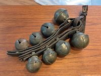 Top view of antique sleigh bells and leather strap showing eight metal bells attached to the worn leather strap with buckle.
