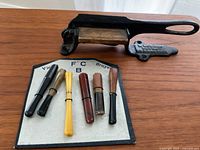 Photo showing antique tobacco cutter and six cigarette holders displayed on a labeled board