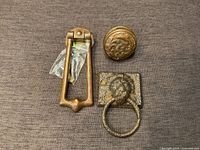 Top view of three antique Victorian hardware pieces: round door knob, rectangular door knocker, horse tie ring on square plate.