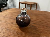 Purple spherical perfume bottle with clear stopper upright on wooden table