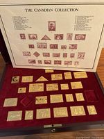 Overview of open wooden display case showing burgundy velvet tray holding multiple silver stamp replicas and reference placard titled 'The Canadian Collection'