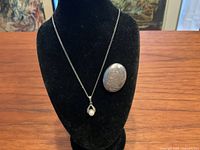 Photo of necklace displayed on a black velvet bust with an oval sterling silver brooch beside it on wooden surface.