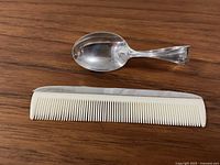 Top view of sterling silver baby spoon and white baby comb with silver topping on wood surface