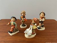 Front view of four Hummel figurines with detailed clothing and accessories