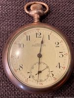 Front view of watch face, white dial with black Arabic numerals and red minute markers