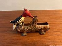 Side view of the vintage woodpecker toothpick holder showing the red-headed woodpecker attached on log-shaped metal base with legs.