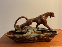 Side view of ceramic panther lamp showing standing panther figure and mottled brown and green glazed base with openings for light elements.