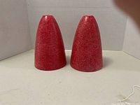 Photo of two retro red fiberglass lamp shades standing upright showing textured surface and conical shape.