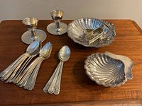 Full view of lot on wooden table showing egg cups, shell dishes, napkin rings, and spoons.