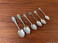 Top view of the six sterling silver Canadian teaspoons with enamel shield designs and maple leaf motifs.