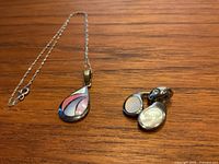 Sterling silver necklace chain with teardrop pendant and matching clip-on earrings on wooden surface.