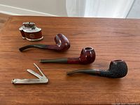 View showing all items on wooden table: three Brigham pipes, retro lighter, and pipe tamper