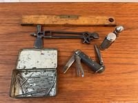 All items displayed on a wooden table showing the multi tool, pocket knife, level, tin with pins, and two small metal containers.