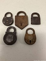 Top view of five varied antique padlocks arranged on white surface, showing front and details clearly.
