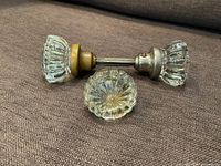 Pair of Victorian style glass door knobs connected with a metal spindle, one single twelve-sided glass door knob placed next to them on brown fabric.