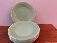 Stack of eight pale green jade-ite Fire King plates with one plate standing upright showing ribbed border