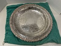 Top and angled view showing ornate embossed floral and scroll decoration on tray surface and raised scalloped rim with intricate detailing.