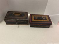 Two vintage metal lock boxes side by side on a white surface showing painted patterns and handles.
