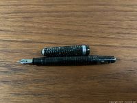 Striped black and silver-tone vintage fountain pen, uncapped, showing the nib.