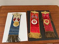 Three vintage medals/badges with silk ribbons laid on table, showing full front view.