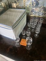 Lot of small and medium size liquor glasses on countertop next to packing container.