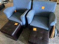Two blue fabric upholstered chairs and two brown leather-type fabric square ottomans on carpeted floor.