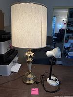 Full view of two table lamps, one tall brass lamp with fabric shade, one smaller white adjustable lamp on desk