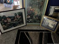 Three framed pictures leaning on wall on carpet: large house on water print, floral painting, smaller house on water print