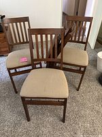 Front view of three wooden folding chairs with beige cushioned seats.