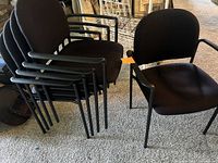 Set of 5 black stackable fabric chairs with metal frames and armrests seen in stacked and individual positions.