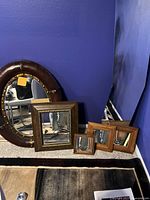 Image shows 6 mirrors of various sizes and frame styles arranged against a blue wall on a carpeted floor.
