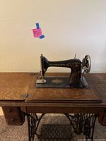 Front view of antique Singer sewing machine on top of wooden desk showing decorative gold and red detailing and Singer branding.