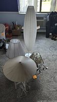 Tall white floor lamp with textured surface and elongated oval shape next to other lamps and shades on carpeted floor
