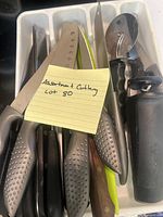 Top view of assorted cutlery including knives and a pizza cutter in a white plastic cutlery holder with a note labeled 'Assorted Cutlery Lot 80'.