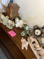 Wide view of lot showing wooden elephant bookends, cream carved elephant bookends, turtle planter, ceramic dog figurine, ornate clock, and small greenish figure