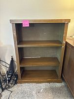 Front view of the brown wood bookshelf showing three shelves and overall wear.