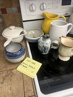Photo showing four ceramic pitchers and three bowls on kitchen countertop and stovetop, illustrating different sizes, shapes, and colors.