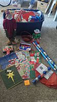 Full lot contents arranged on floor with large blue plastic storage bin, showing stuffed figures, gift wrap, bags, tissue paper, ornaments, and boxes.