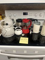 Lot of coffee and tea pots, grinders, and accessories displayed on stove top and counter.
