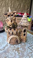 Front view of a ceramic decorative sculpture of a castle with a dragon on top, showing detailed features including eyes, scales, door, and tower roof.
