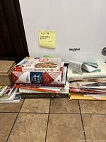 Stack of 7 cookbooks on floor against wall with sticky note labeled 'Cook books Recipes'. Various sizes and conditions visible.