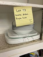 Stack of white square dinner plates with simple black lines on edge, 8 plates visible